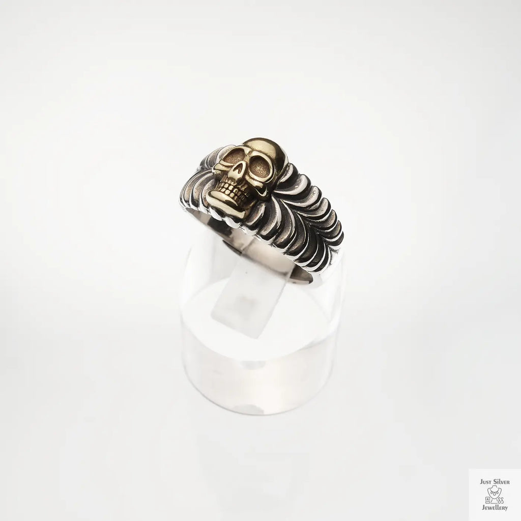 Silver and gold coloured skull ring on a white background