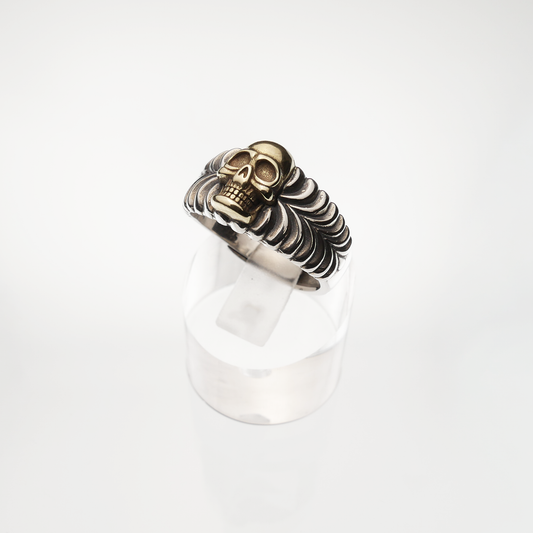 Silver and gold coloured skull ring on a white background