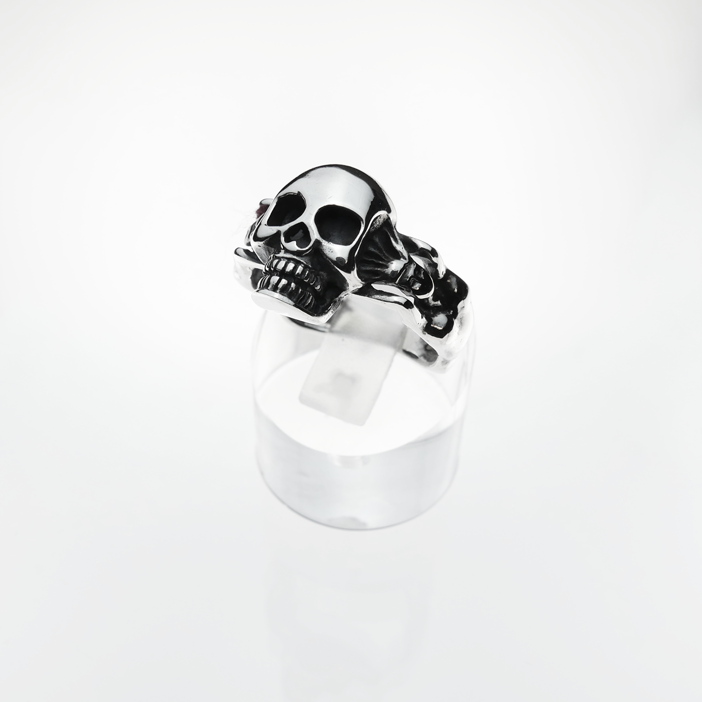 Silver skull ring on a clear stand with a white background