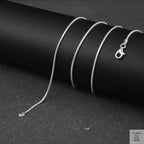 Silver fine snake necklace on a black cylindrical object