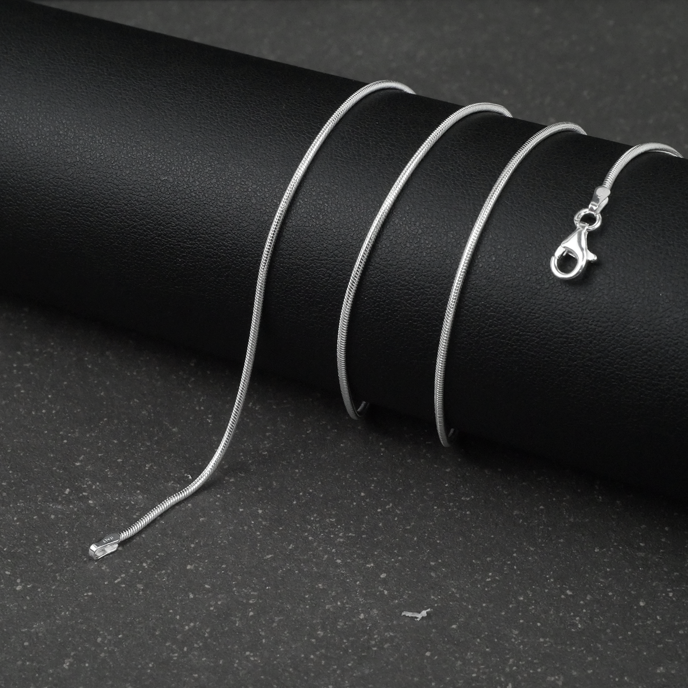 Silver fine snake necklace on a black cylindrical object