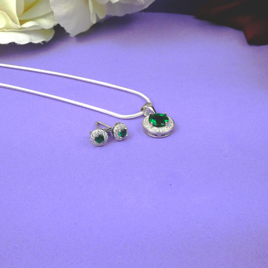 Silver jewelry set with green gemstones on a purple surface with white flowers.