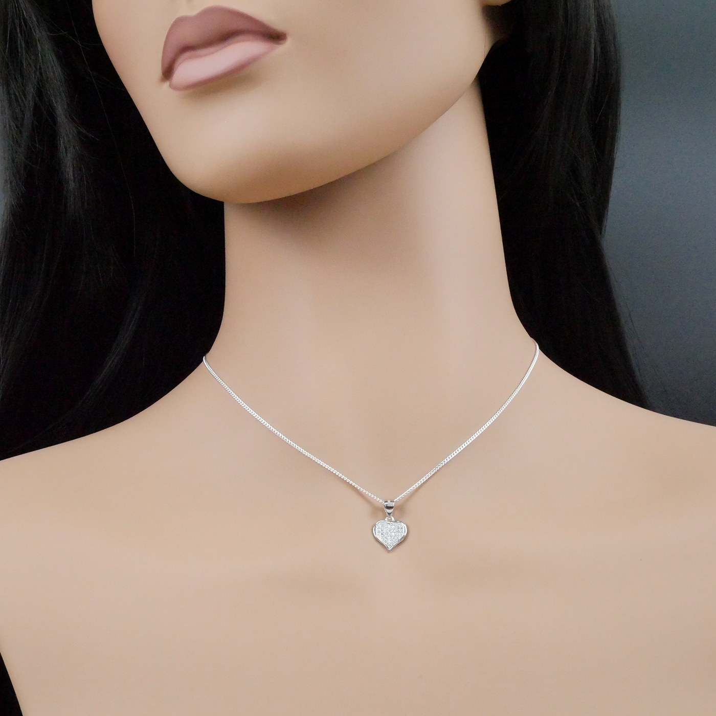 Mannequin wearing a silver necklace with a heart-shaped pendant on a dark background