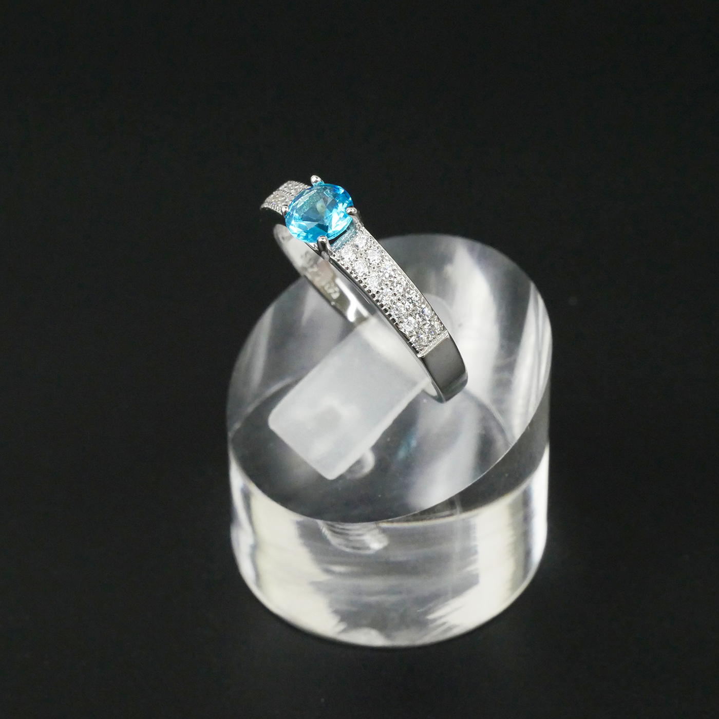Silver ring with a blue gemstone on a clear stand against a black background