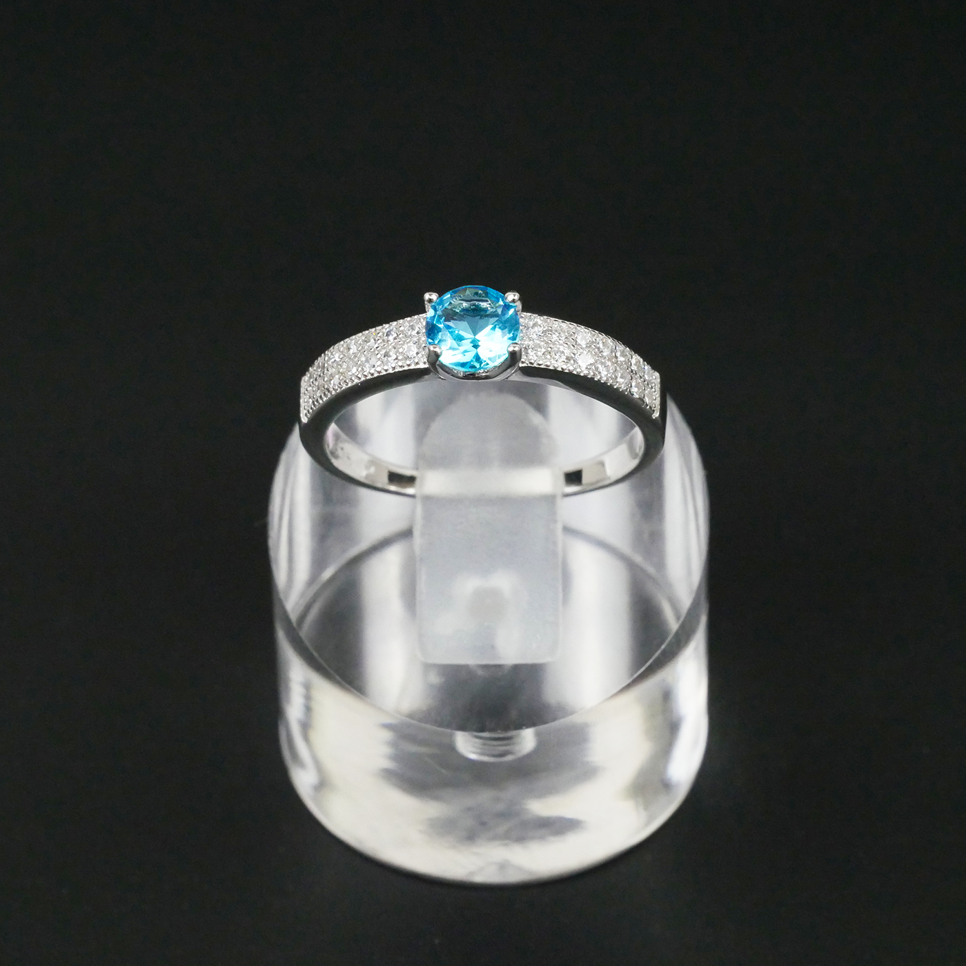 Silver ring with a blue gemstone on a clear stand against a black background