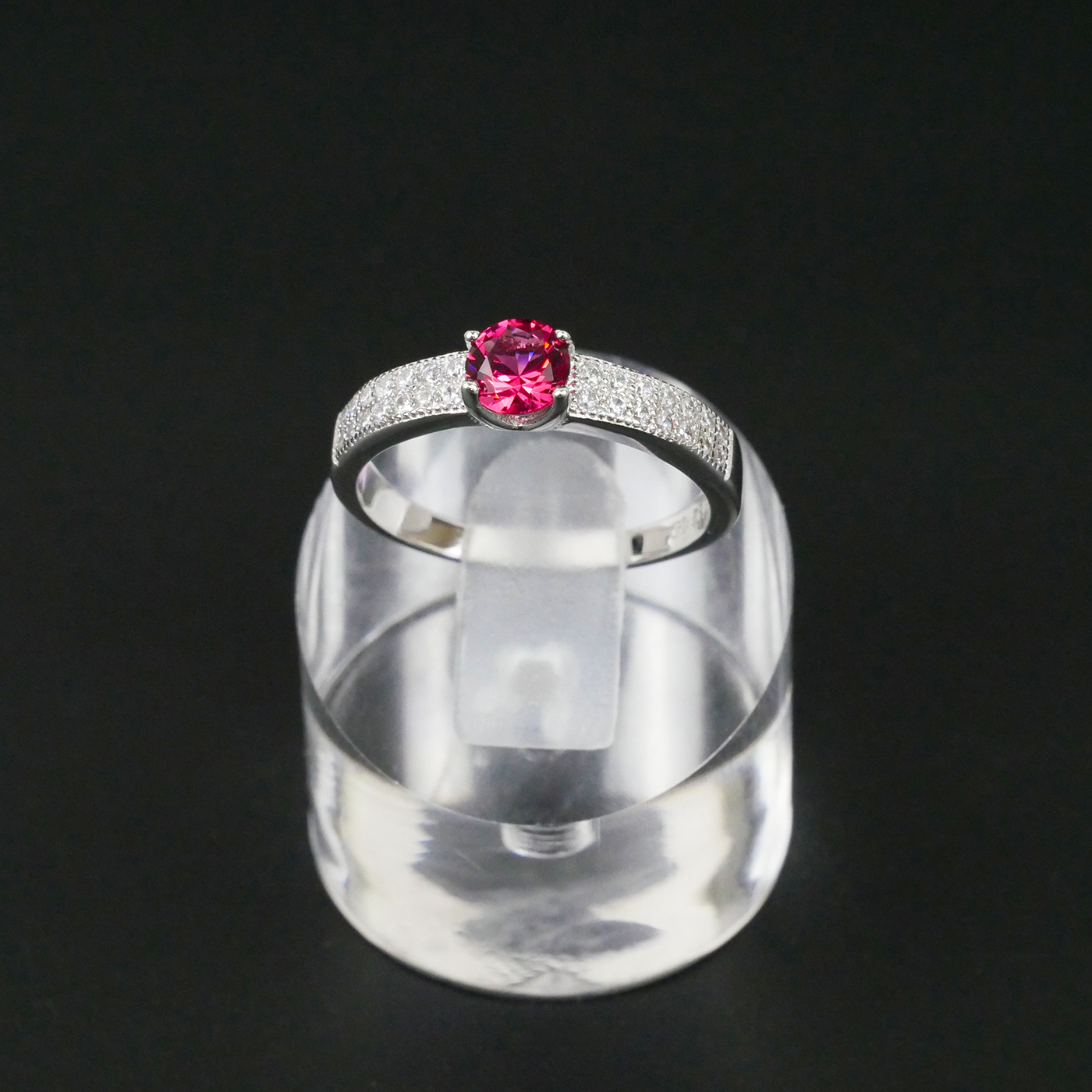 Silver ring with a red gemstone on a clear stand against a black background