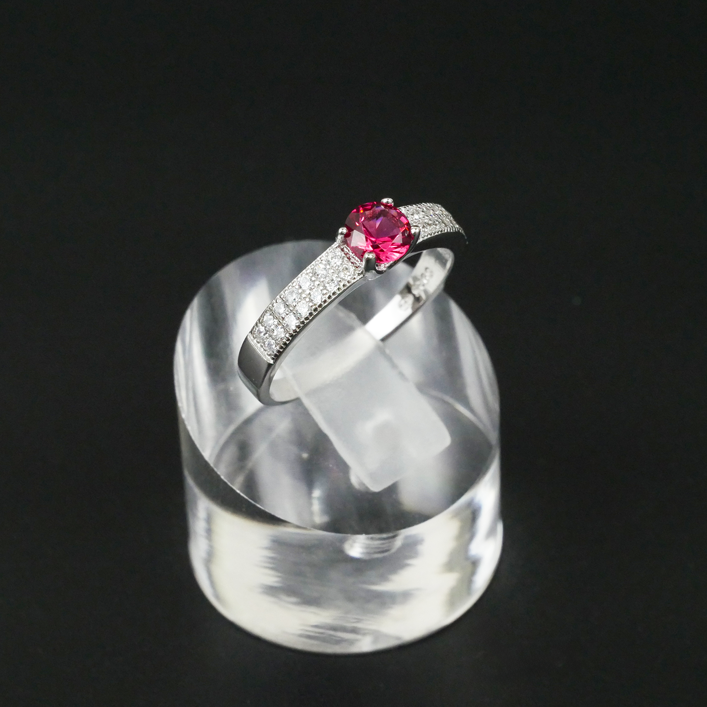 Silver ring with a red gemstone on a clear stand against a black background