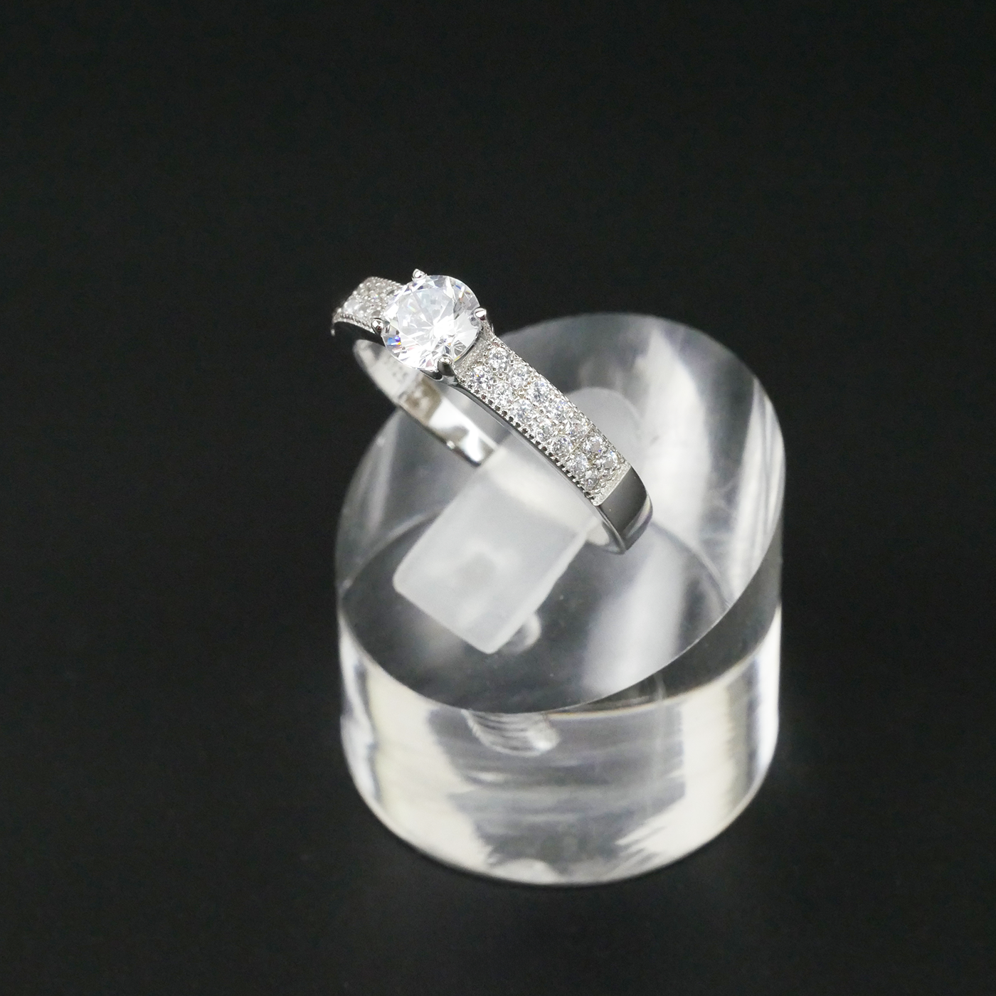 Silver ring with a central CZ on a clear stand against a black background
