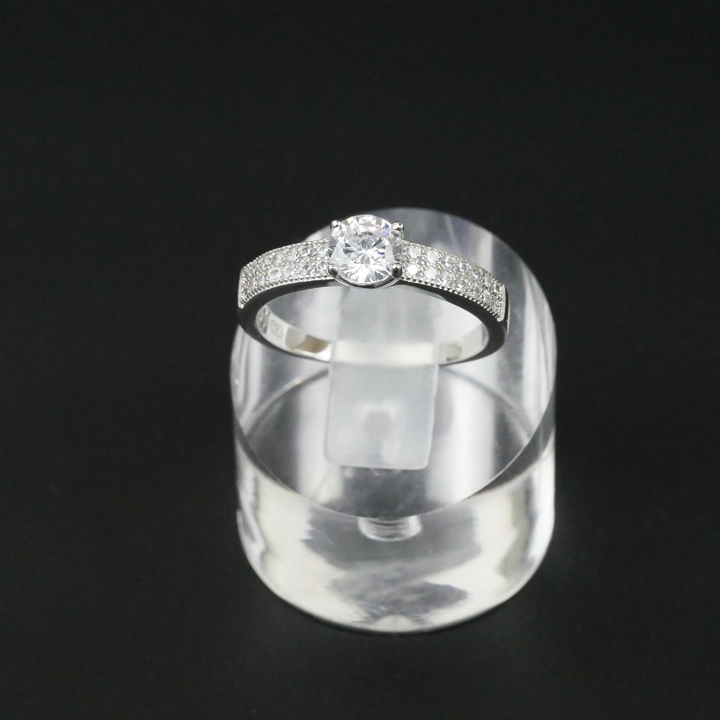 Silver ring with a central CZ on a clear stand against a black background