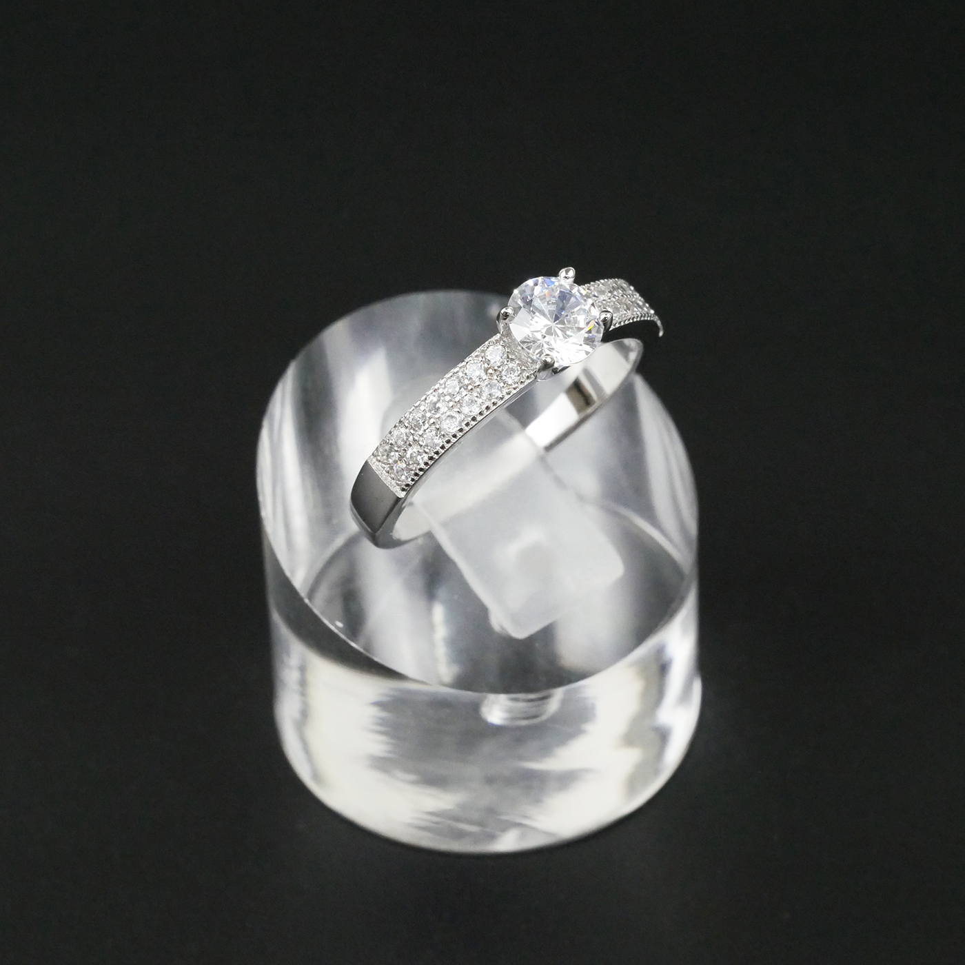 Silver ring with a central CZ on a clear stand against a black background