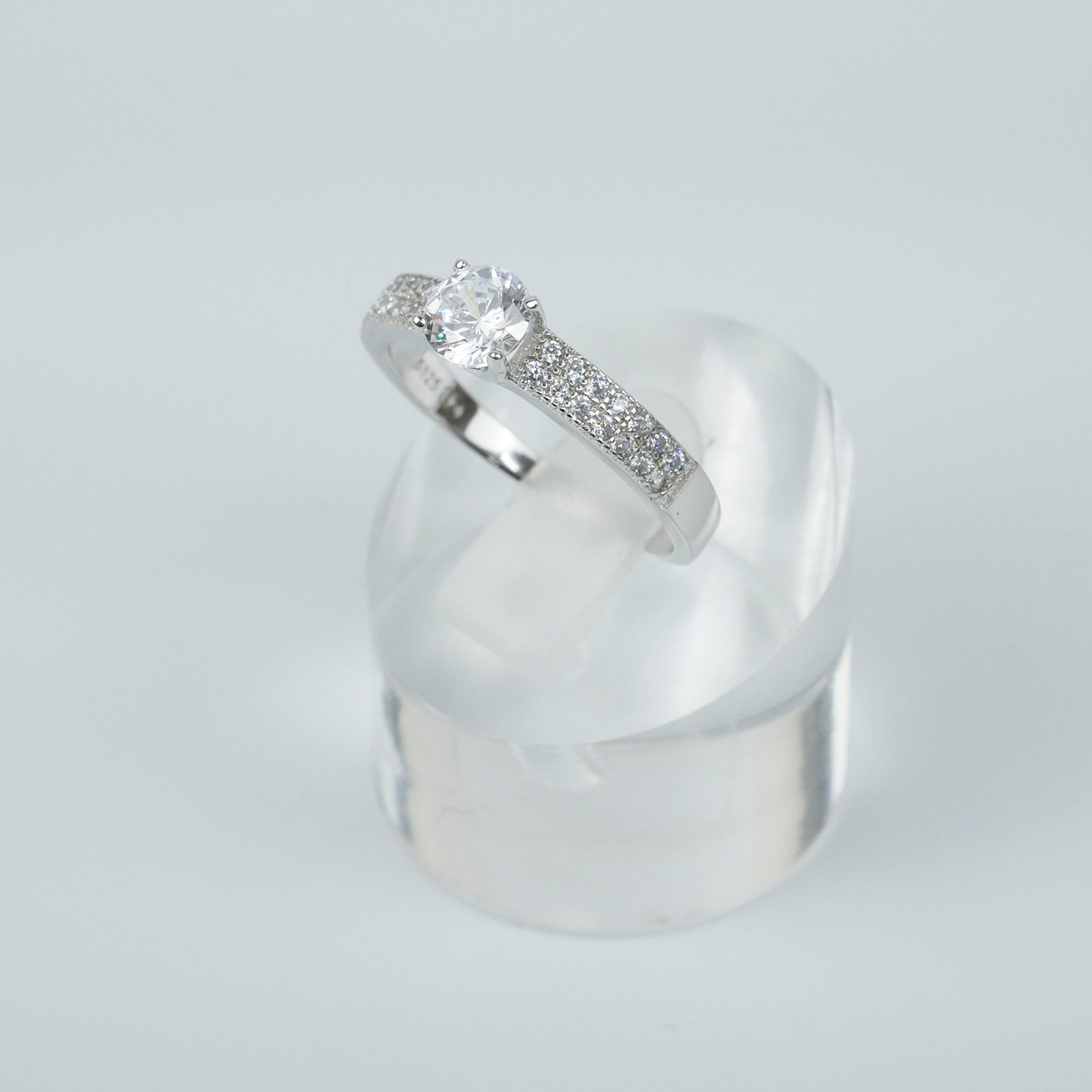Silver ring with a central CZ on a clear stand against a light-grey background