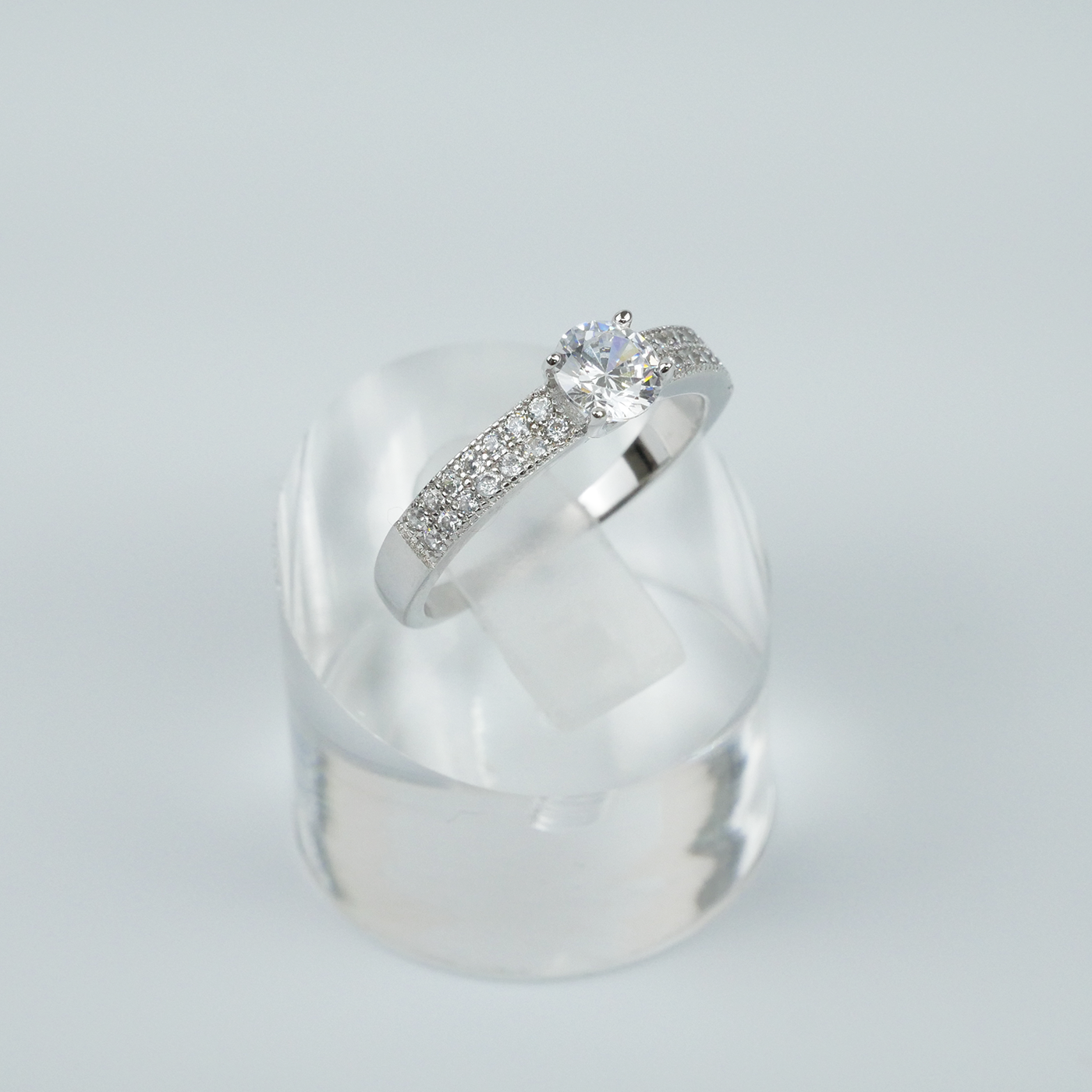 Silver ring with a central CZ on a clear stand against a light-grey background