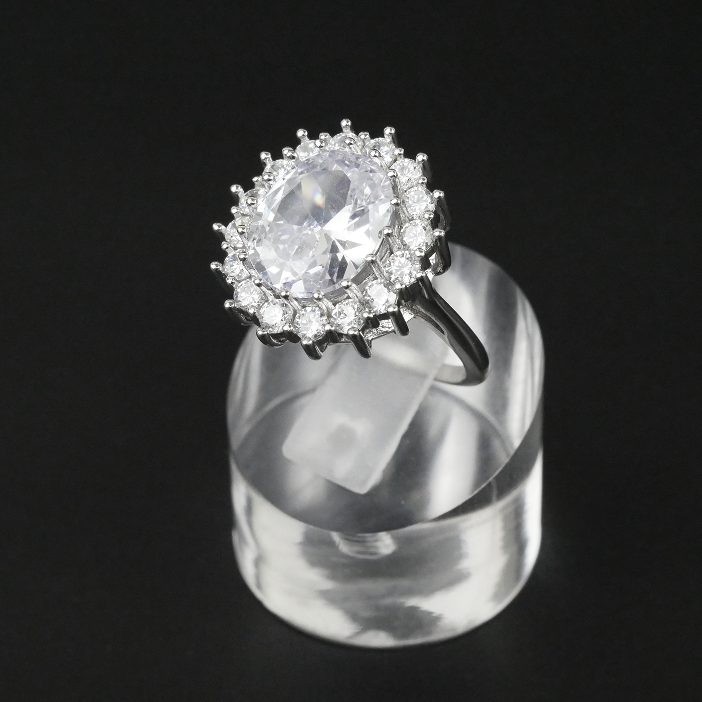 Ring with a white gemstone and CZ-studded halo on a clear stand against a light-grey background