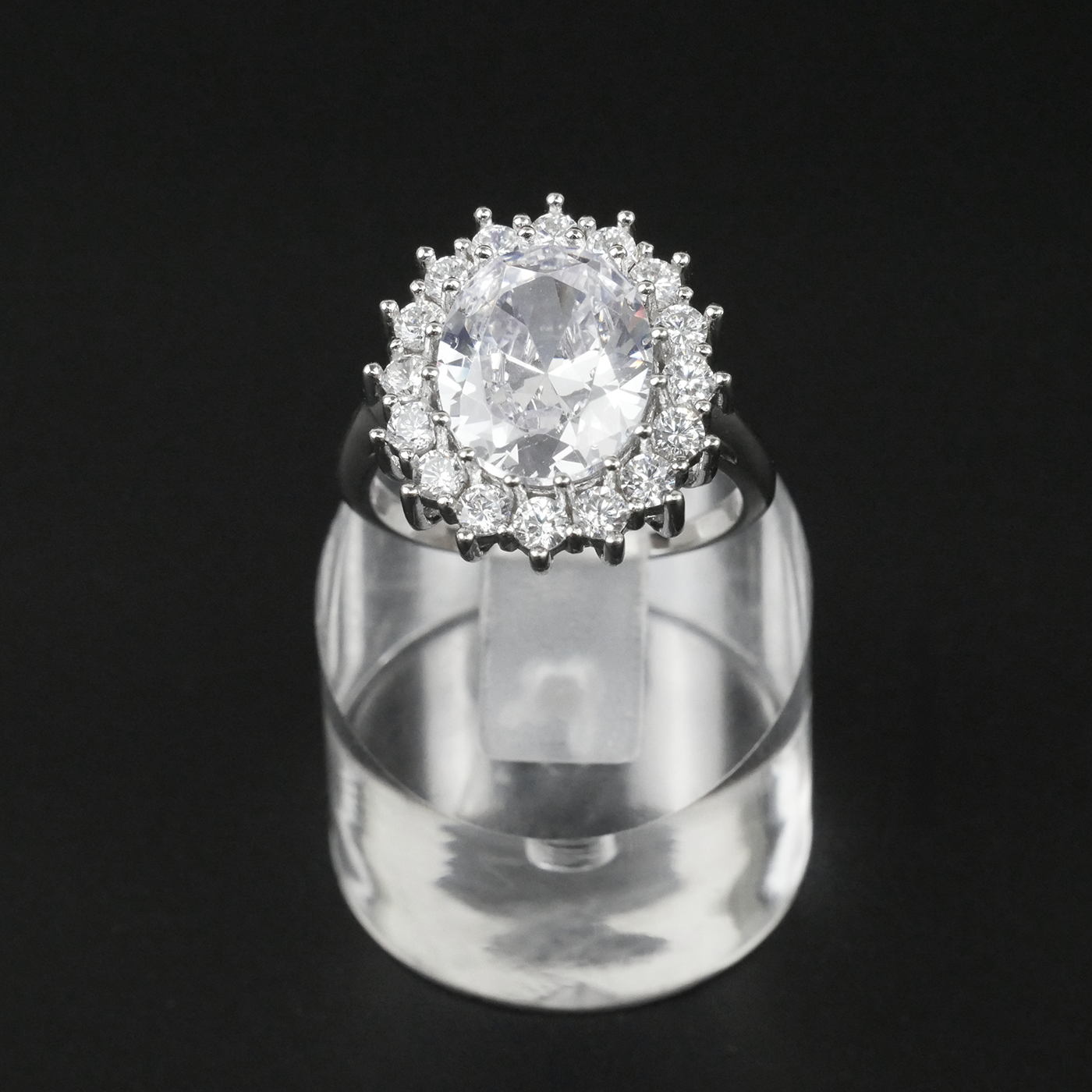 Ring with a white gemstone and CZ-studded halo on a clear stand against a light-grey background