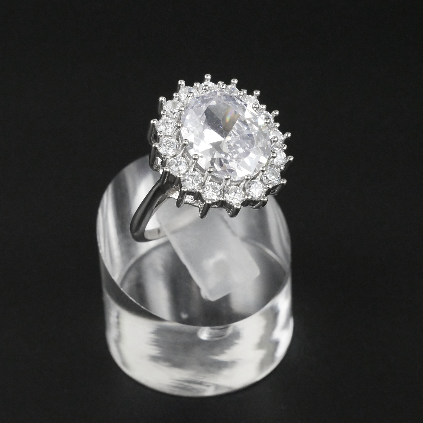 Ring with a white gemstone and CZ-studded halo on a clear stand against a light-grey background