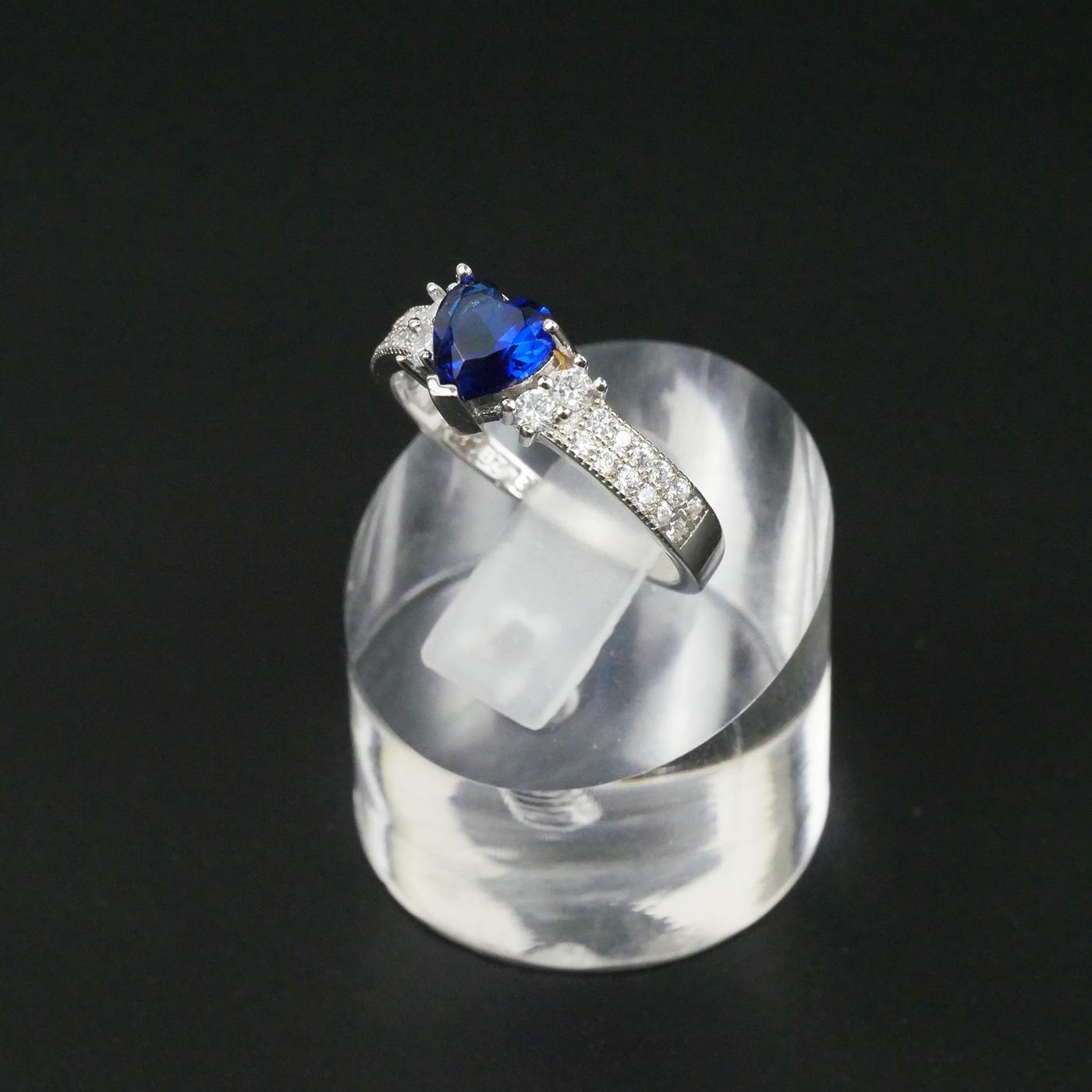 Silver ring with a blue gemstone on a clear stand against a black background