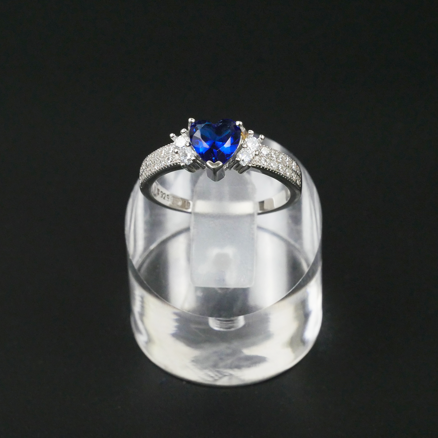 Silver ring with a blue gemstone on a clear stand against a black background