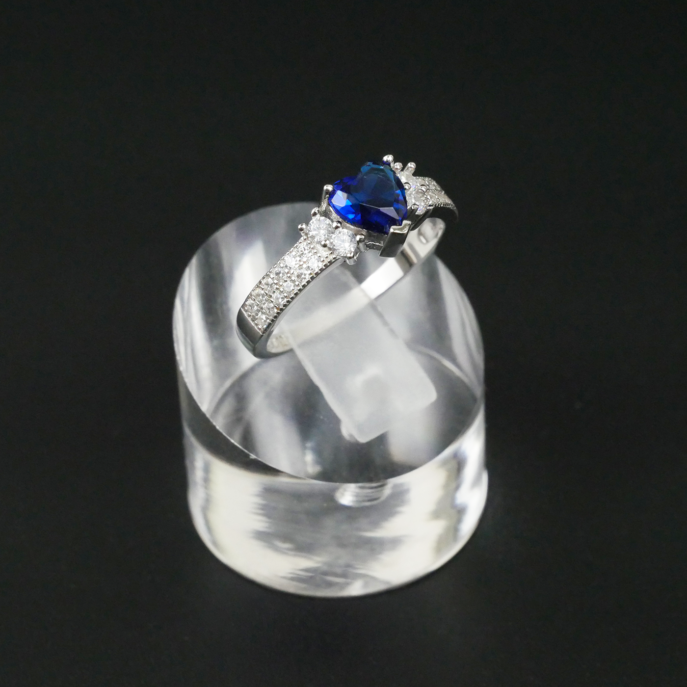 Silver ring with a blue gemstone on a clear stand against a black background