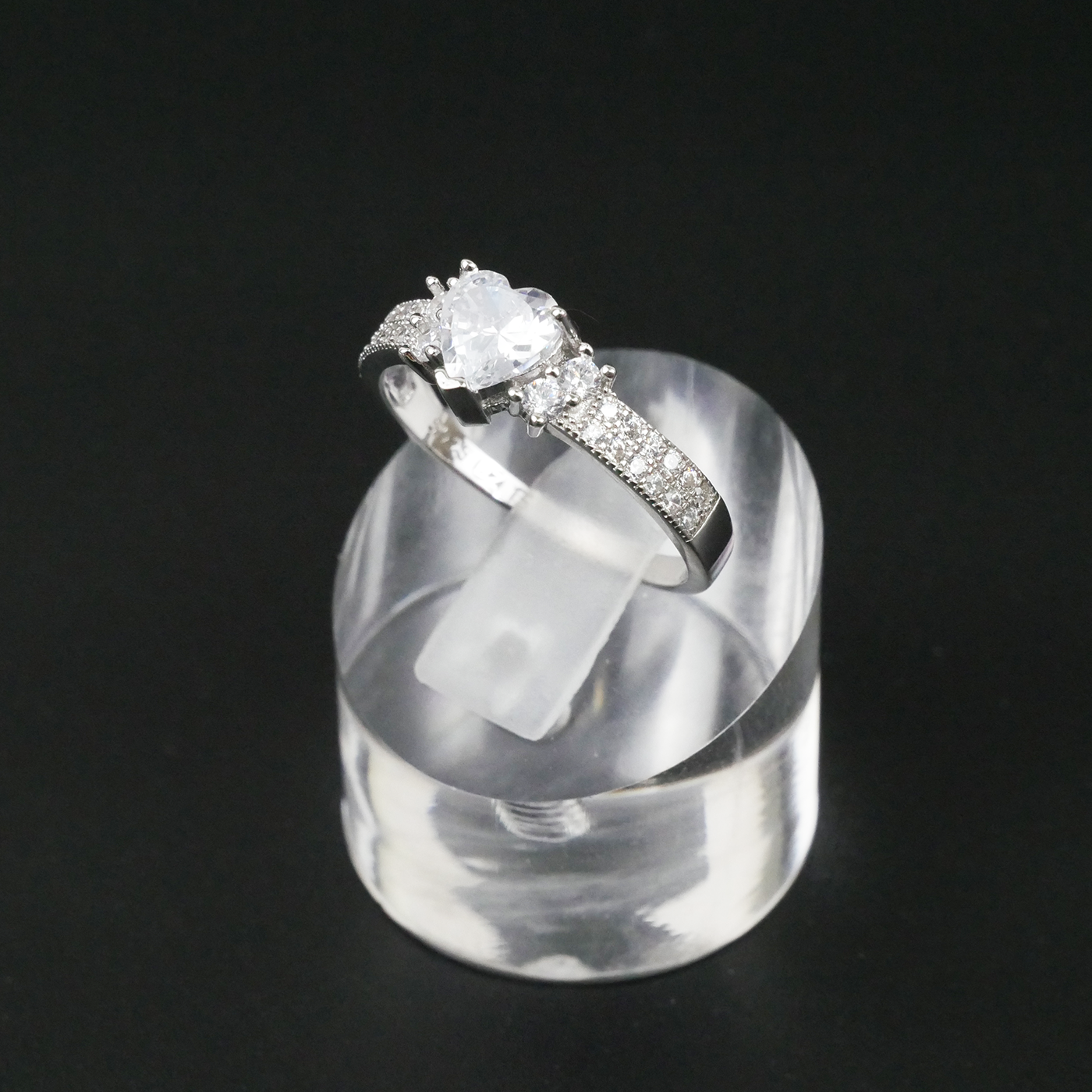 Silver ring with a large central gemstone and smaller stones on a clear stand against a black background