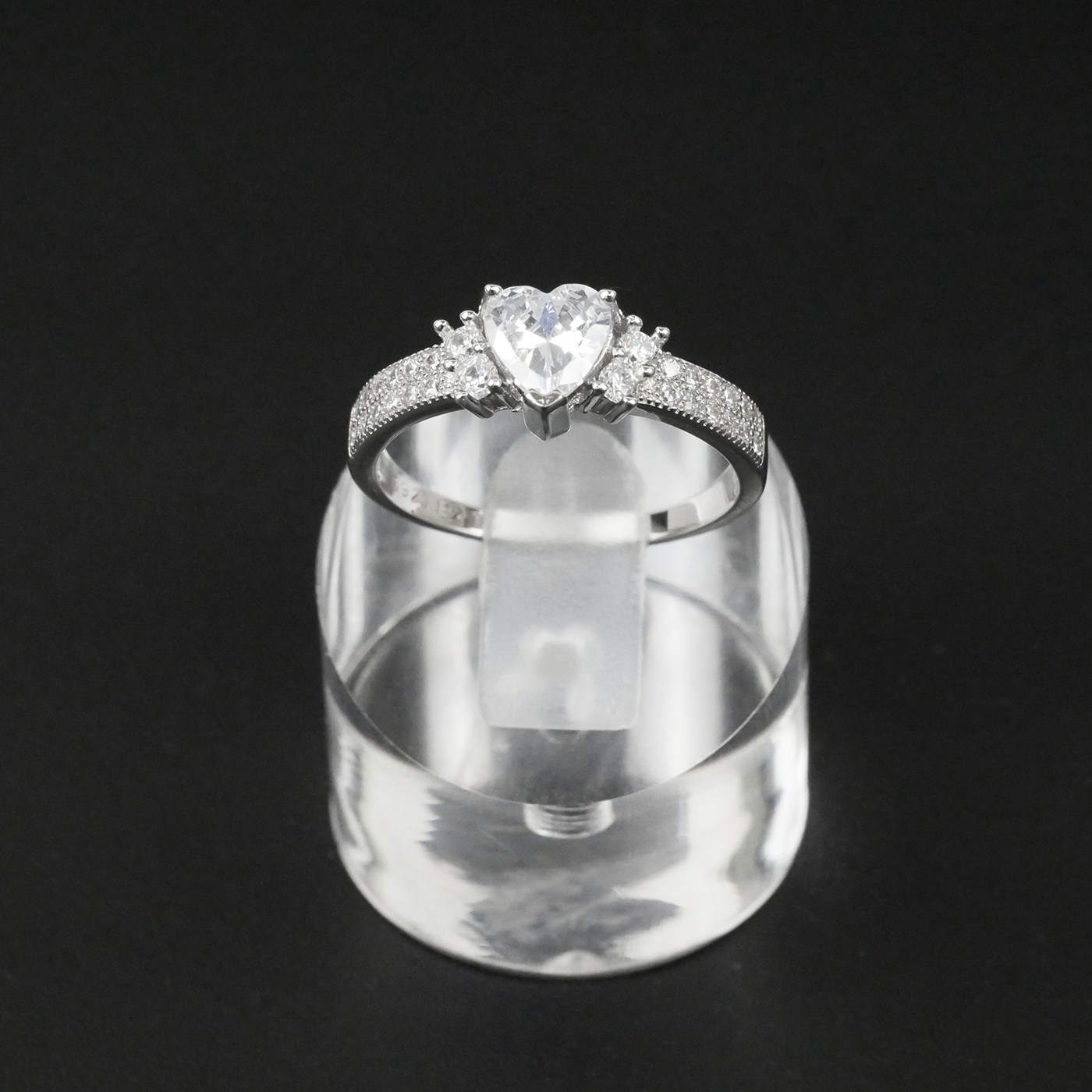Silver ring with a large central gemstone and smaller stones on a clear stand against a black background