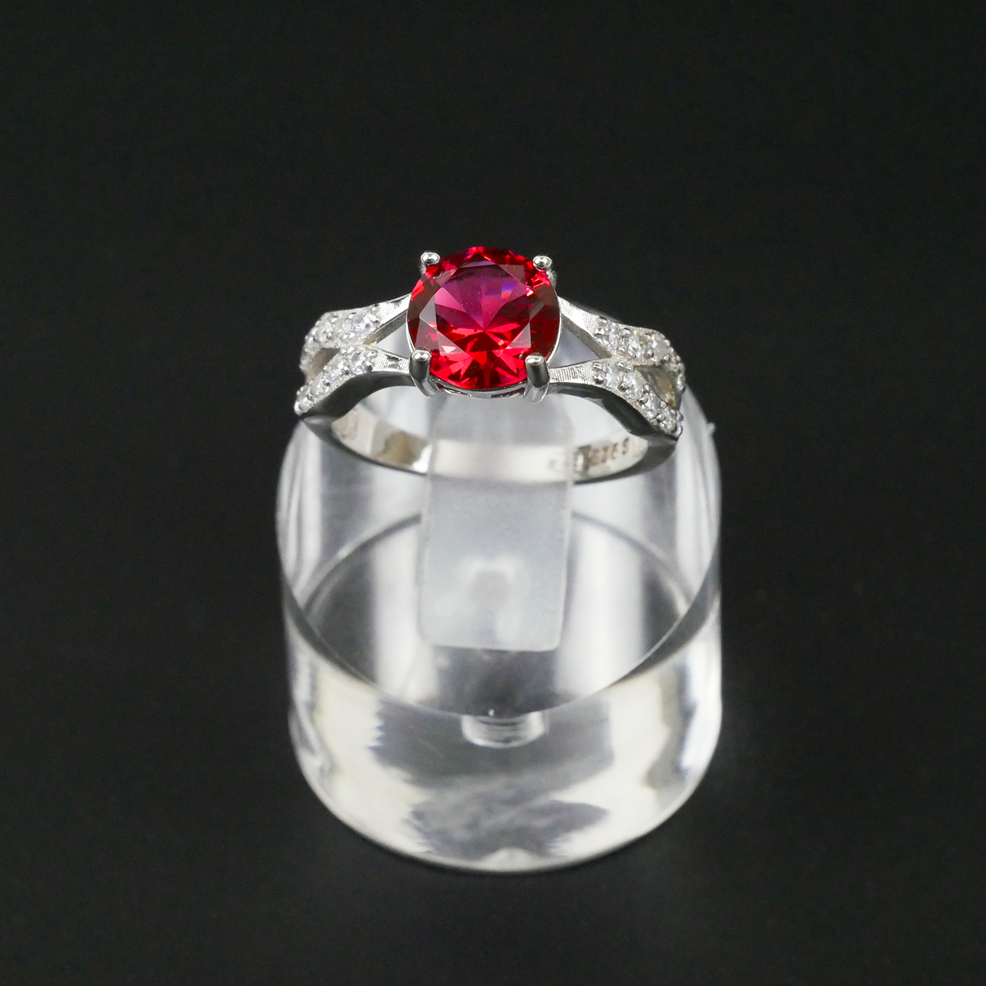 Silver ring with a red gemstone on a clear stand against a black background