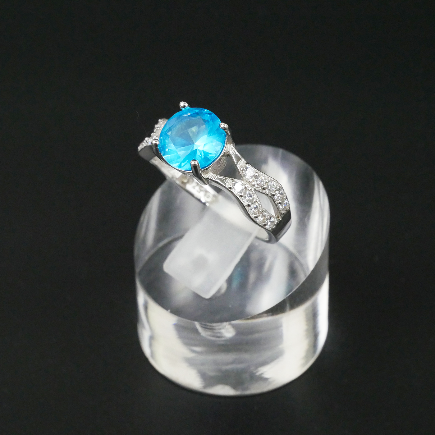 Silver ring with a blue gemstone on a clear stand against a black background