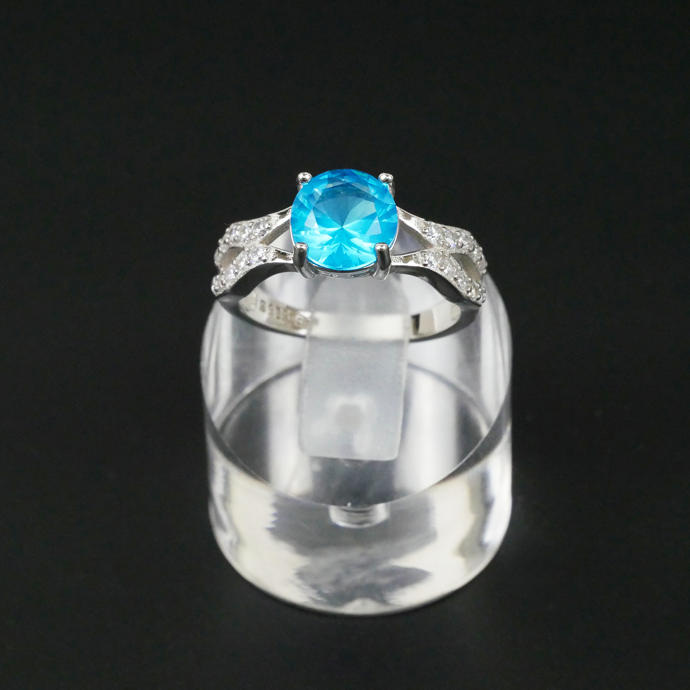 Silver ring with a blue gemstone on a clear stand against a black background
