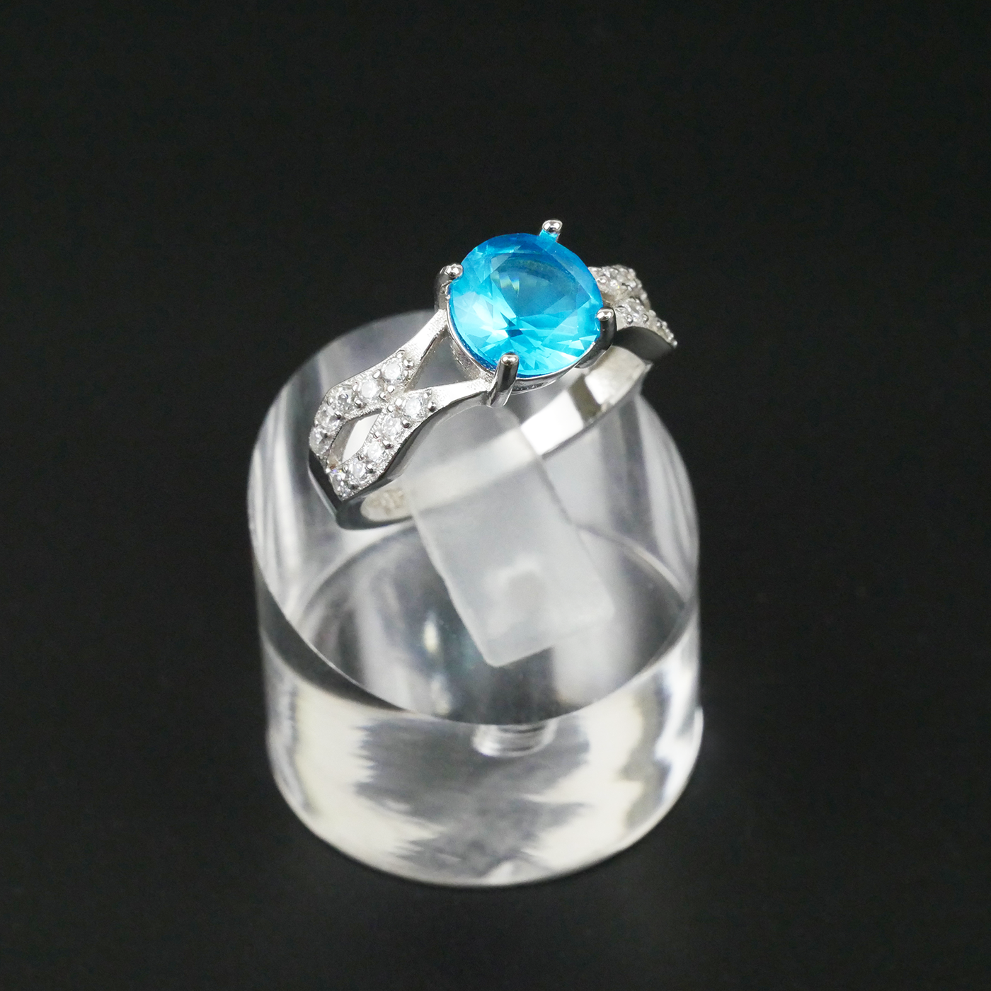 Silver ring with a blue gemstone on a clear stand against a black background