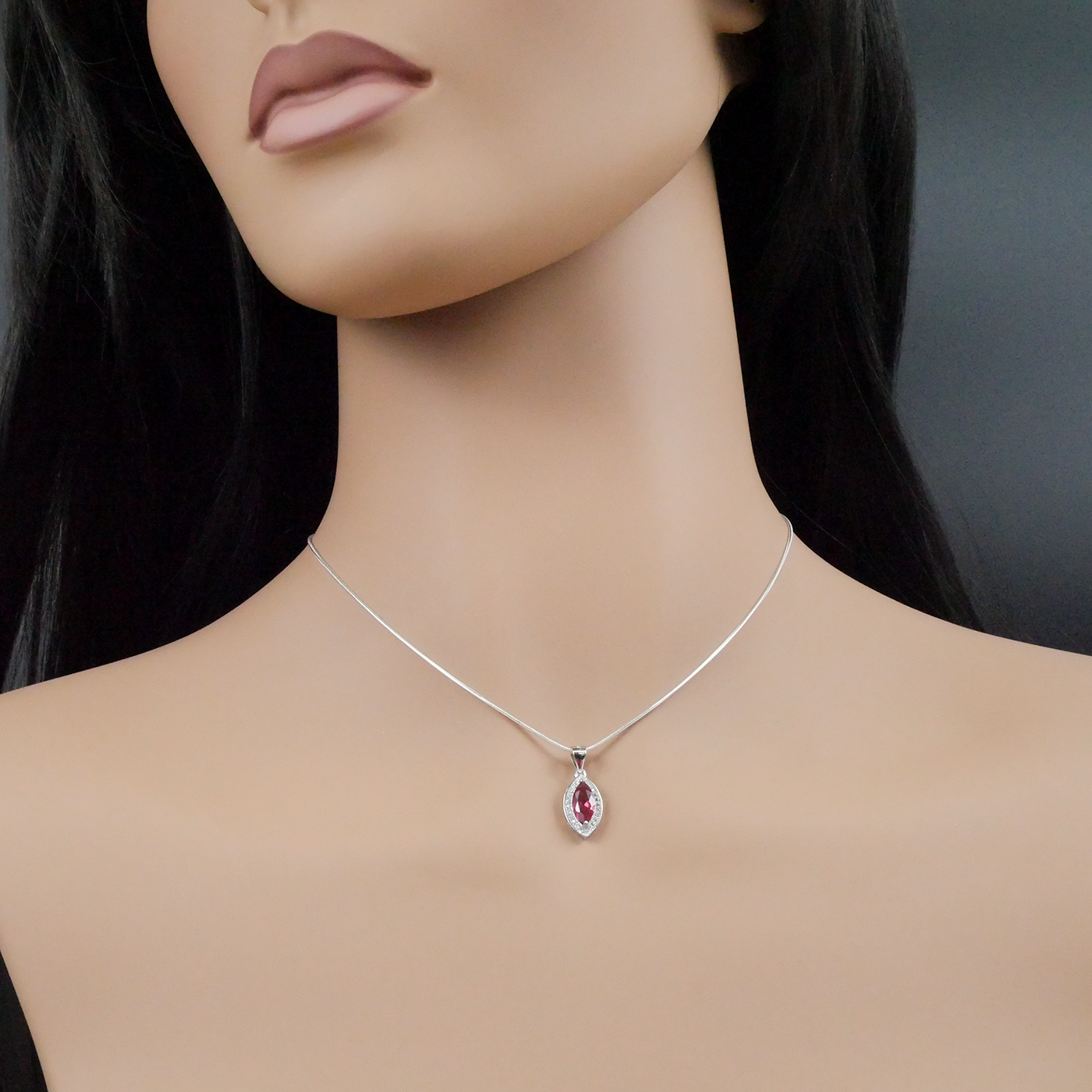 Mannequin wearing a silver necklace with a red pendant on a dark background