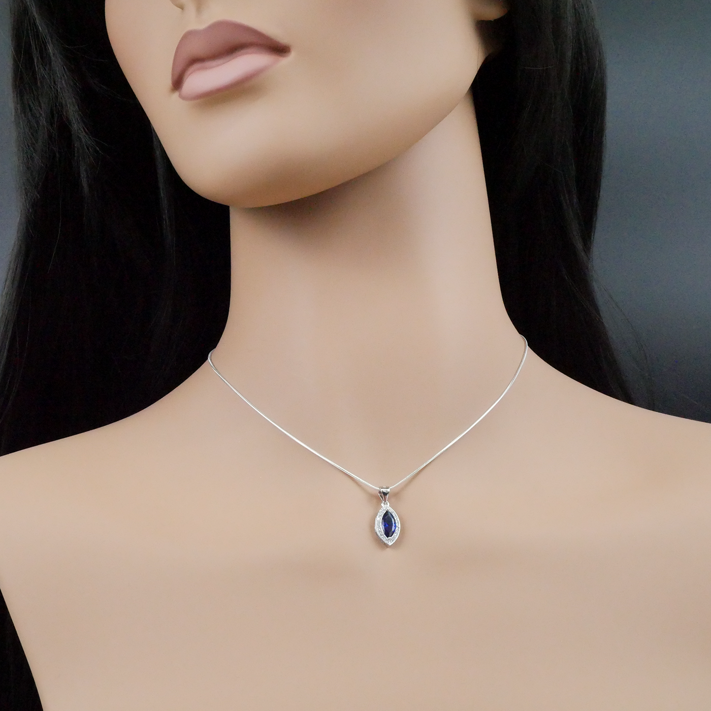 Mannequin wearing a silver necklace with a blue pendant against a dark background