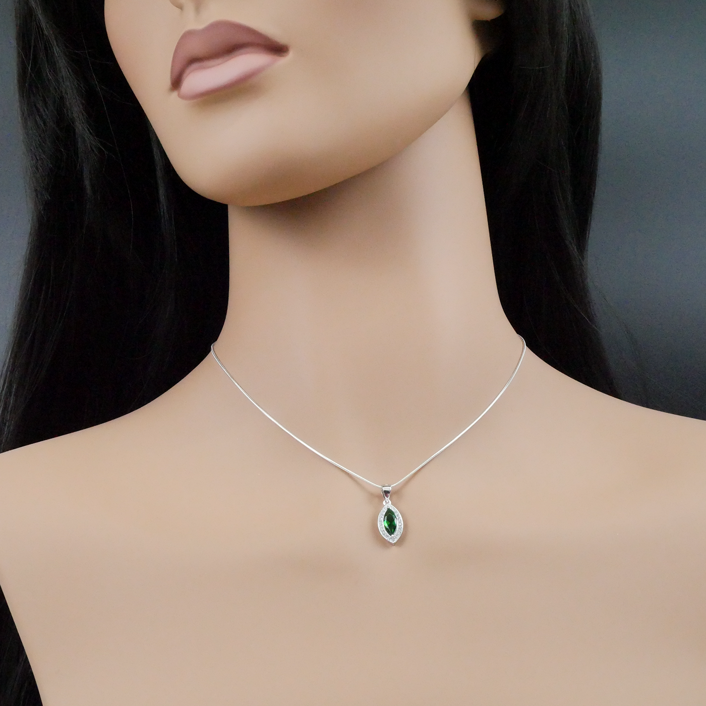 Mannequin wearing a silver necklace with a green pendant against a dark background