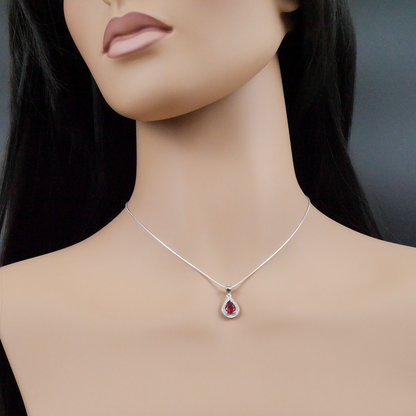 Mannequin wearing a silver necklace with a red teardrop pendant on a dark background