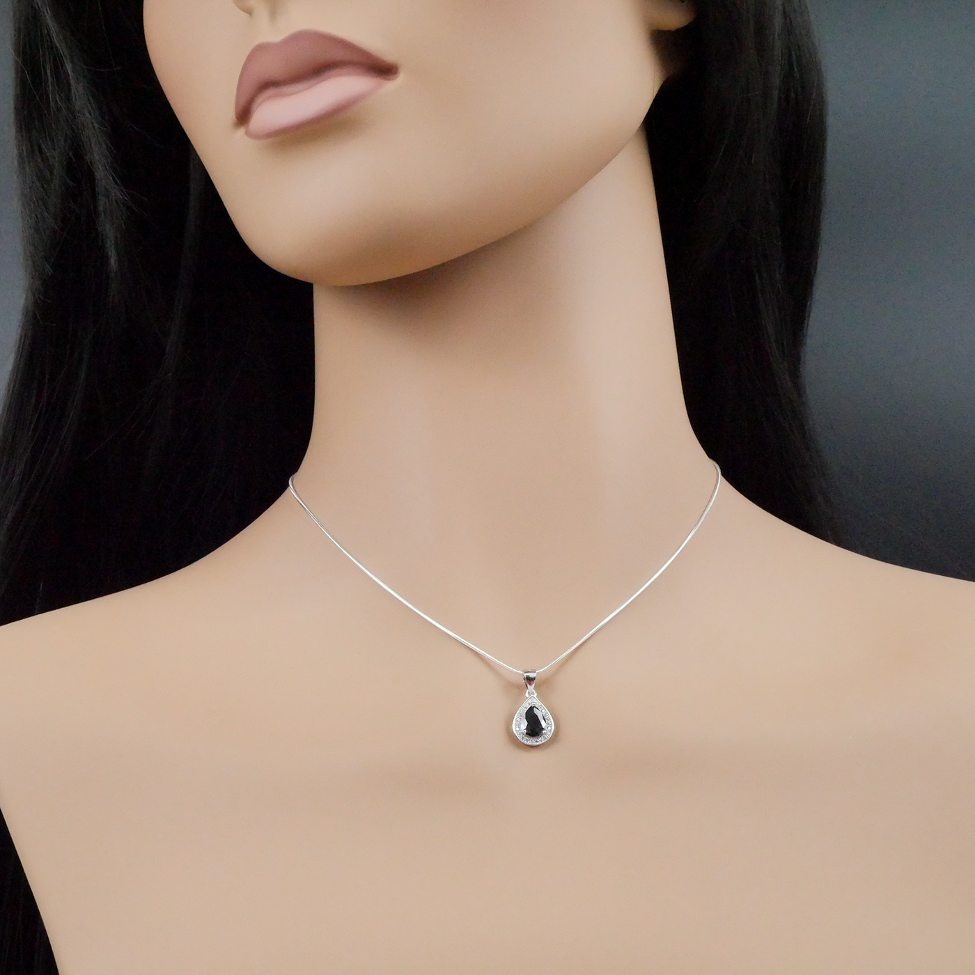 Mannequin wearing a silver necklace with a teardrop pendant on a dark background