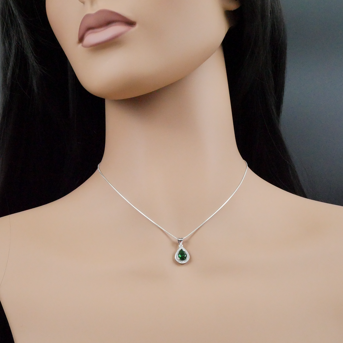Mannequin wearing a silver necklace with a green pendant against a dark background