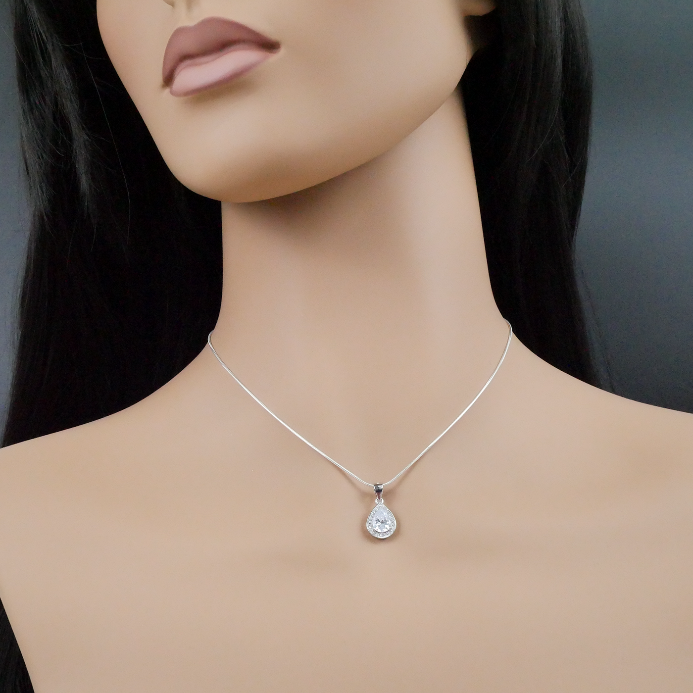 Mannequin wearing a silver necklace with a clear pendant on a dark background