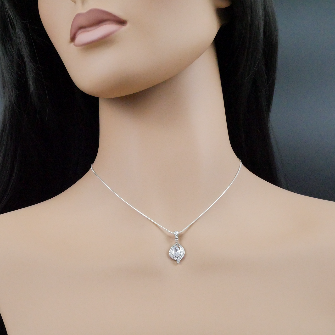 Mannequin wearing a silver necklace with a teardrop pendant on a dark background