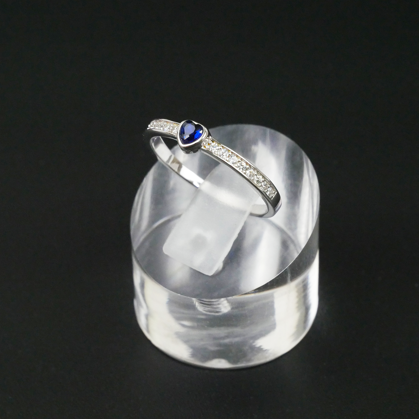 Silver ring with a blue gemstone on a clear stand against a black background