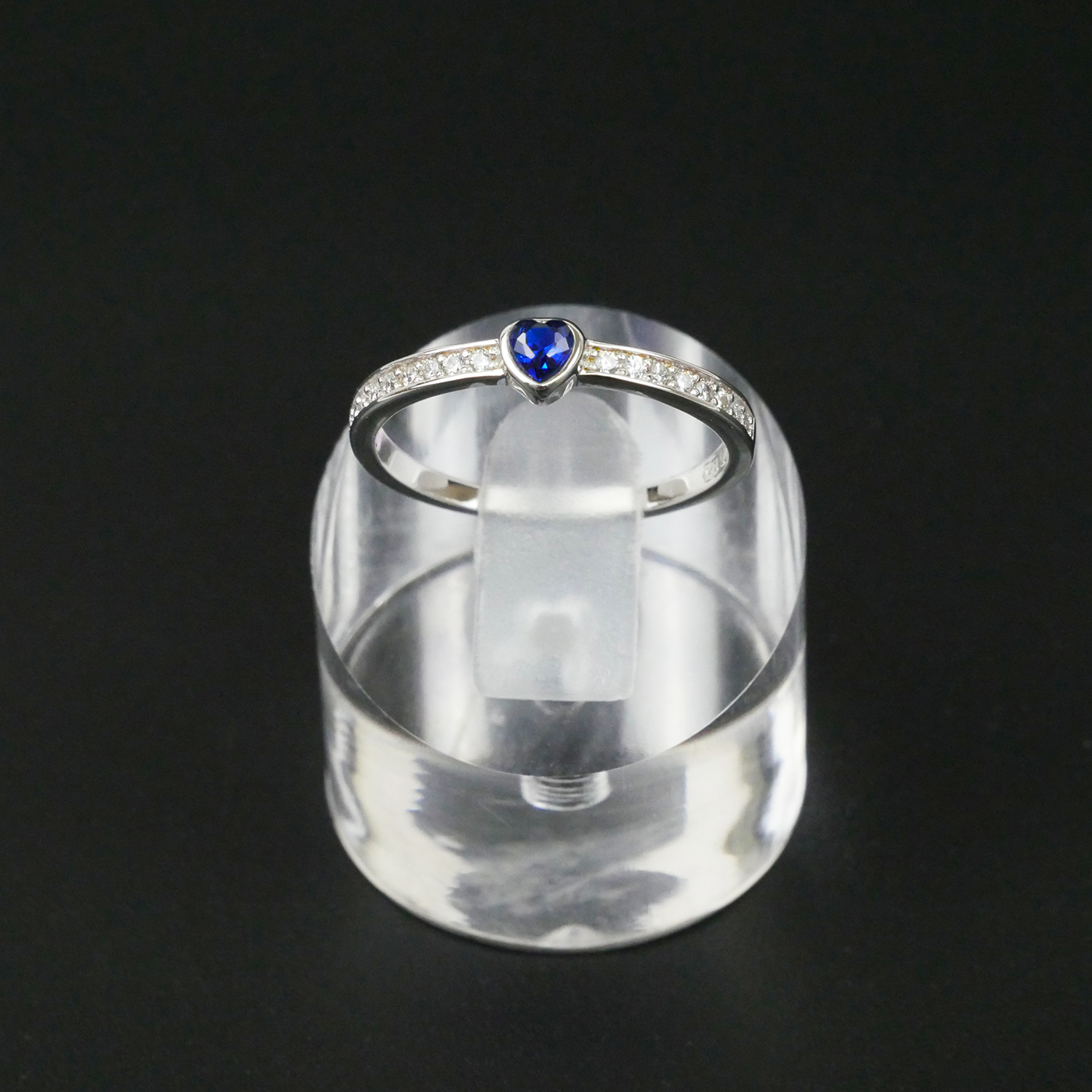 Silver ring with a blue gemstone on a clear stand against a black backgroun