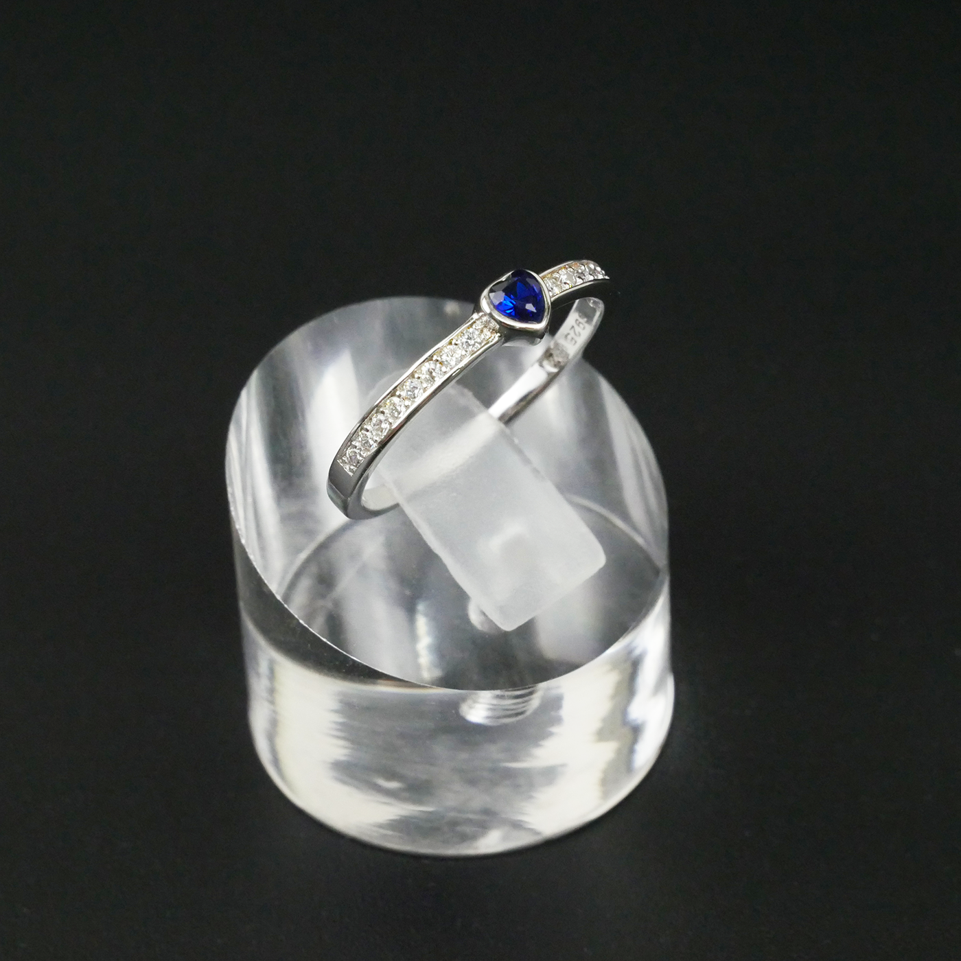 Silver ring with a blue gemstone on a clear stand against a black backgroun