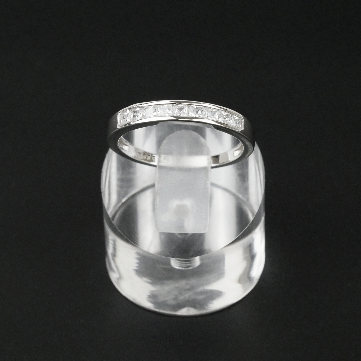 Silver ring on a clear stand against a black background
