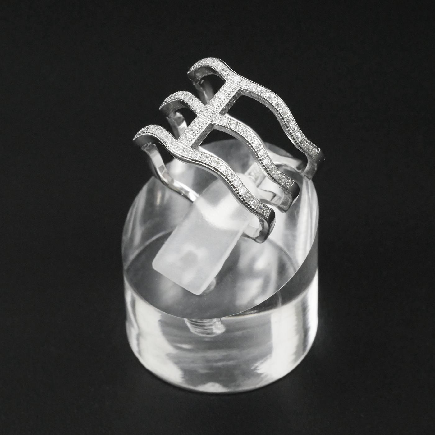 Silver ring with intricate design on a clear stand against a black background