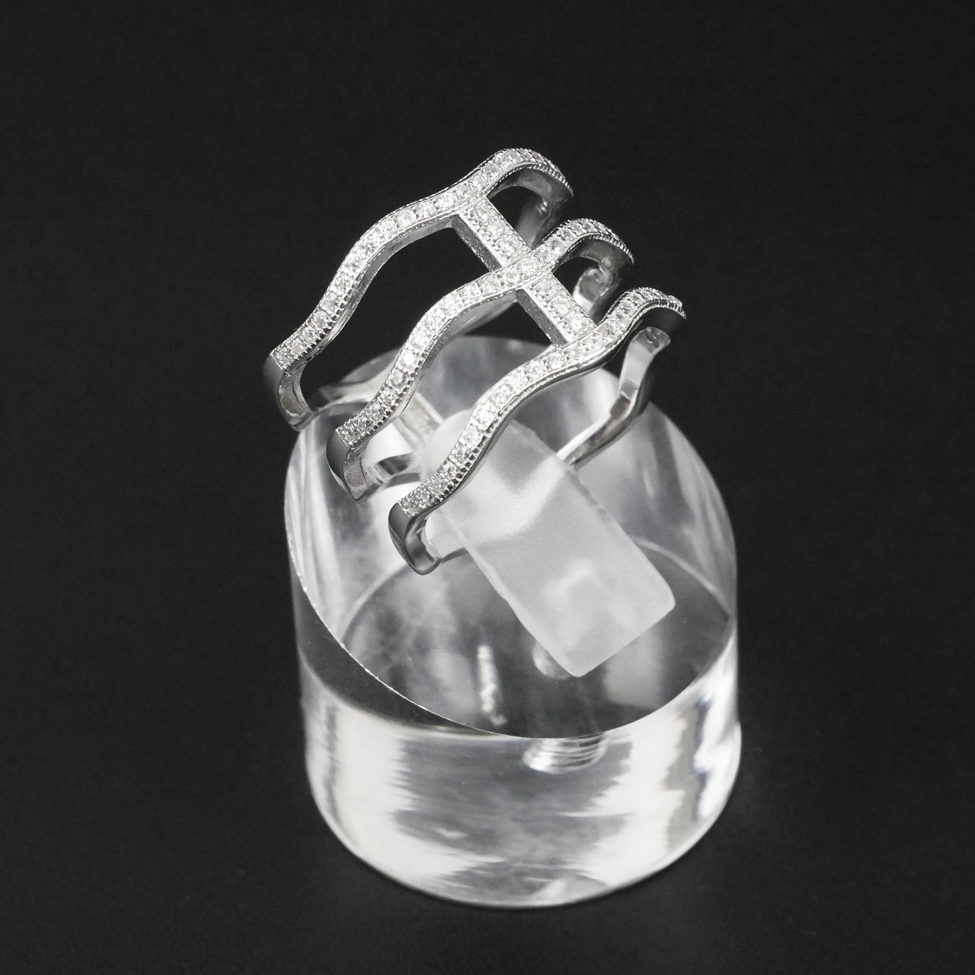 Silver ring with intricate design on a clear stand against a black background