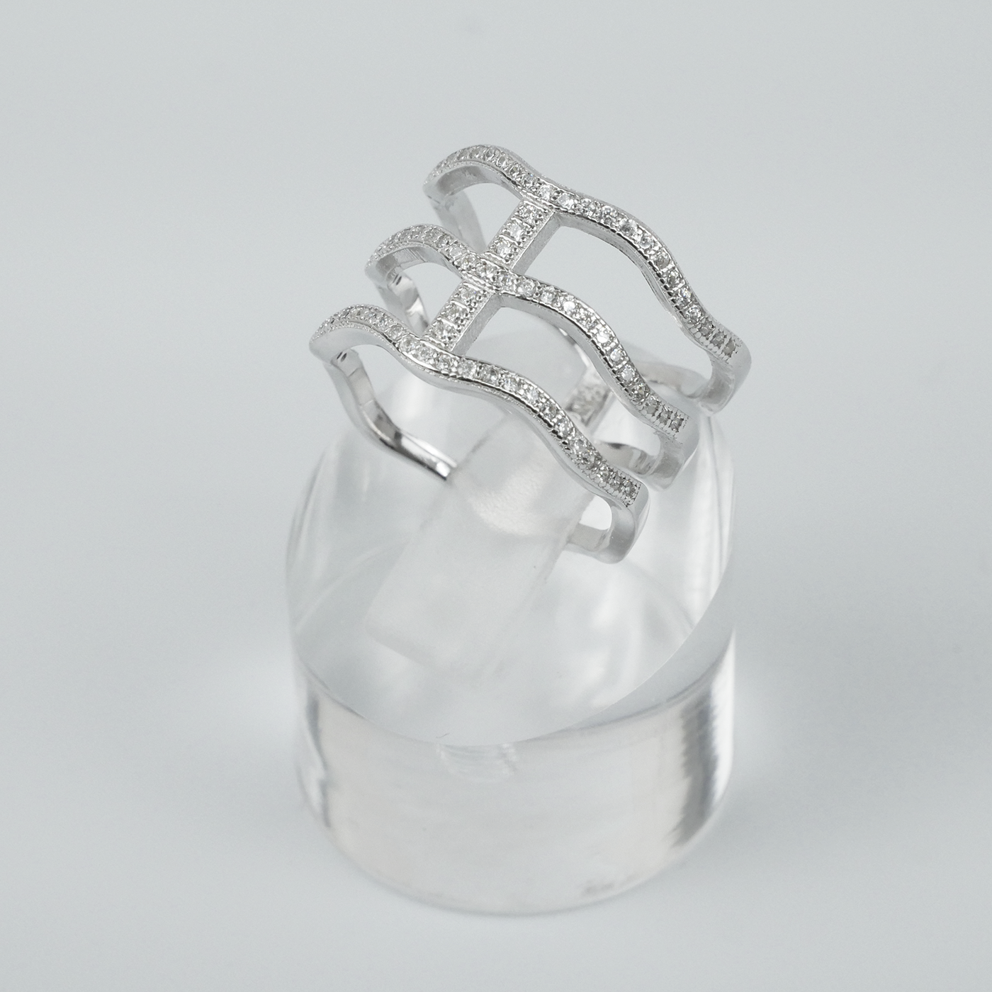 Silver ring with intricate design on a clear stand against a light-grey background