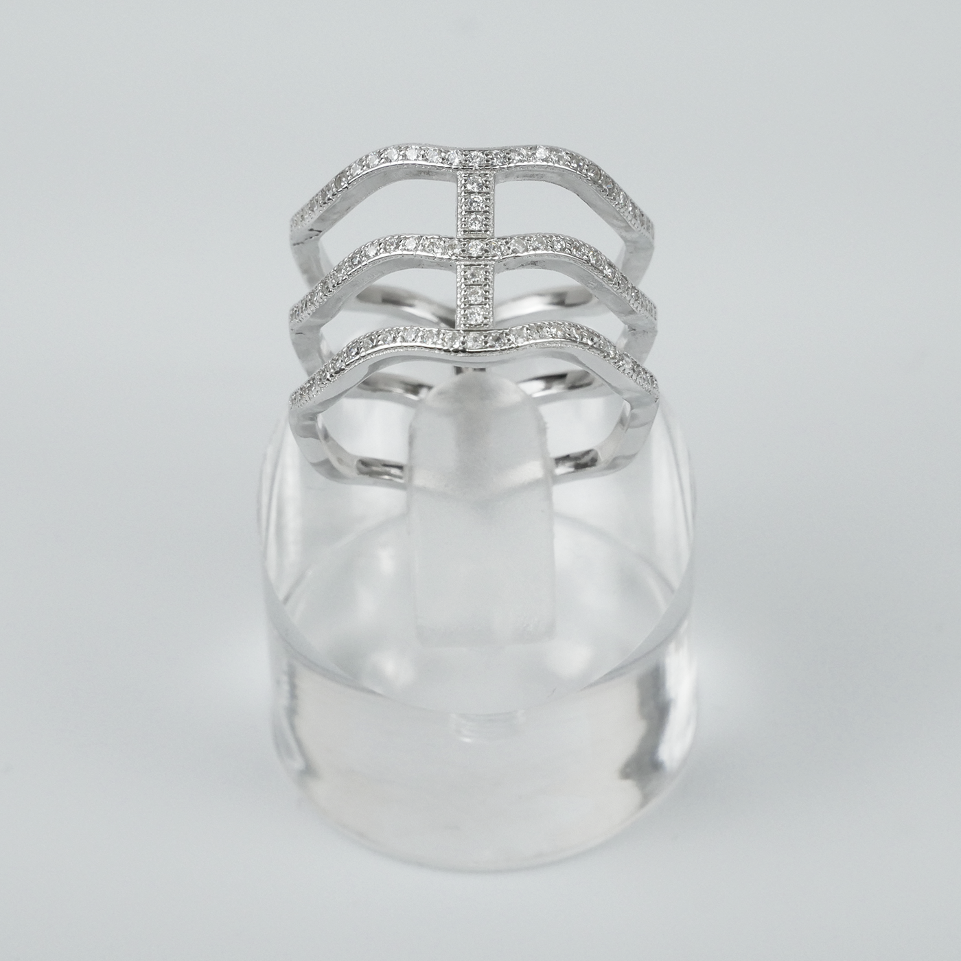 Silver ring with intricate design on a clear stand against a light-grey background