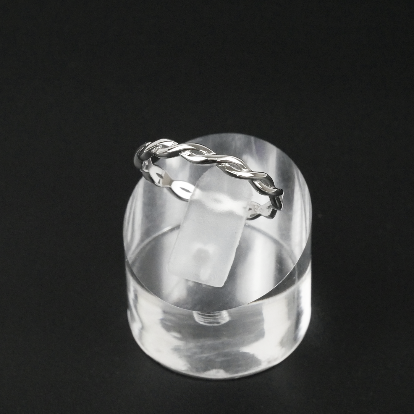 Silver ring with a twisted design on a clear stand against a black background