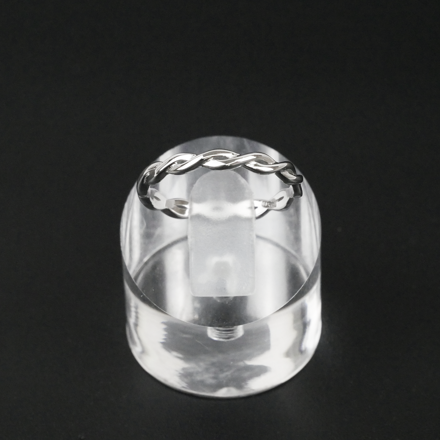 Silver ring with a twisted design on a clear stand against a black background
