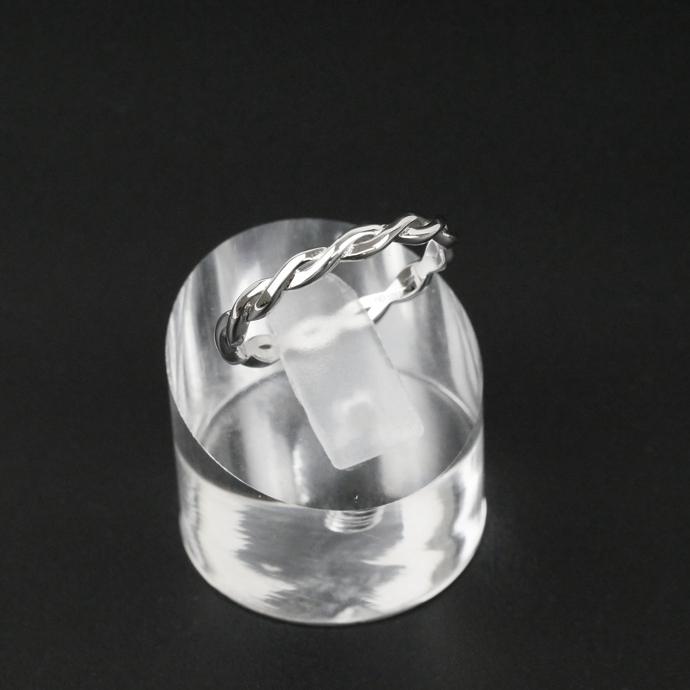 Silver ring with a twisted design on a clear stand against a black background