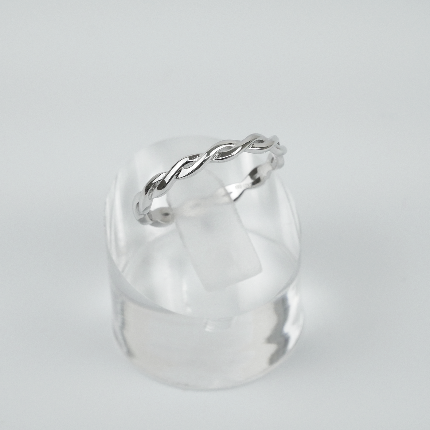 Silver ring with a twisted design on a clear stand against a light gray background
