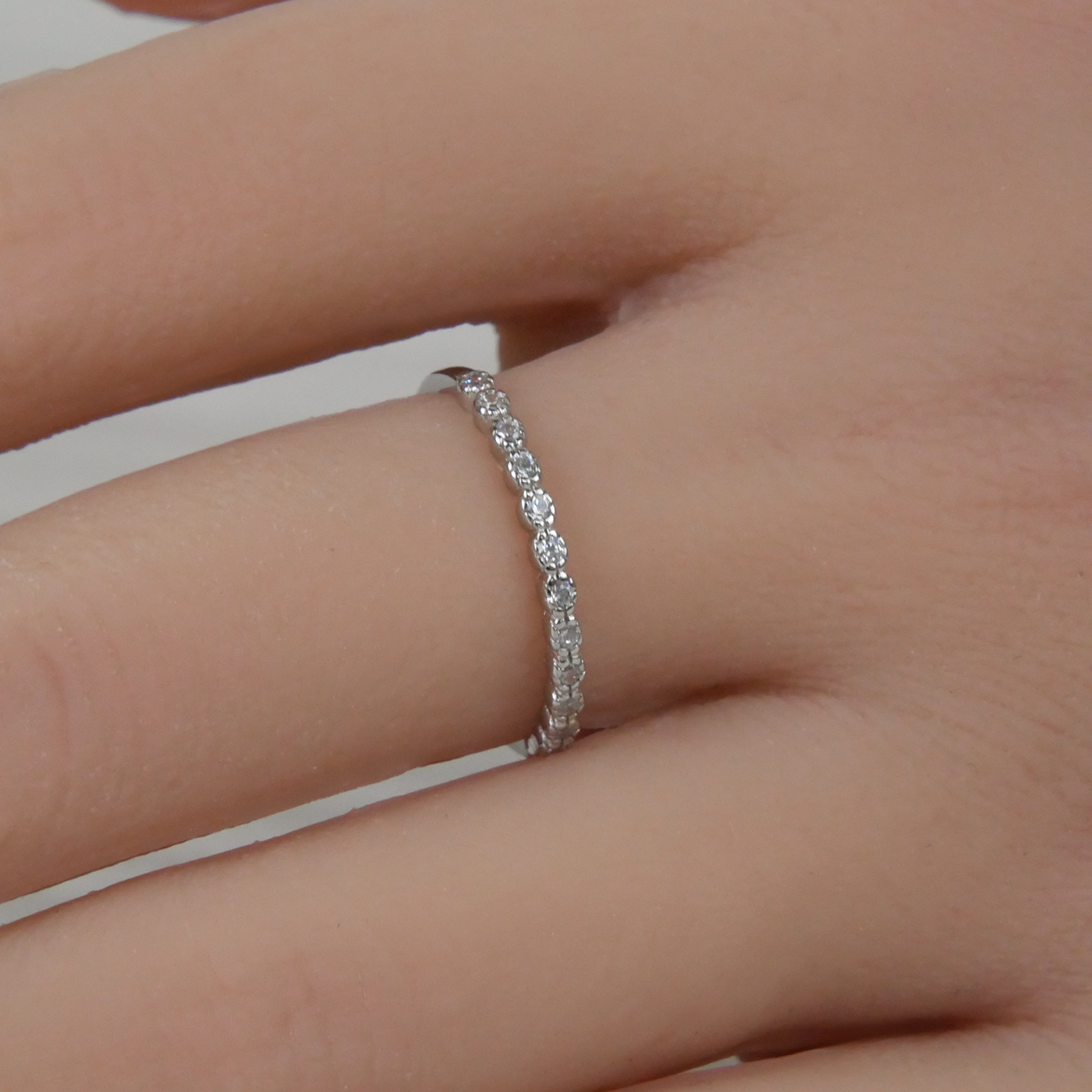 Silver ring with small Zirconia on a person's finger against a neutral background