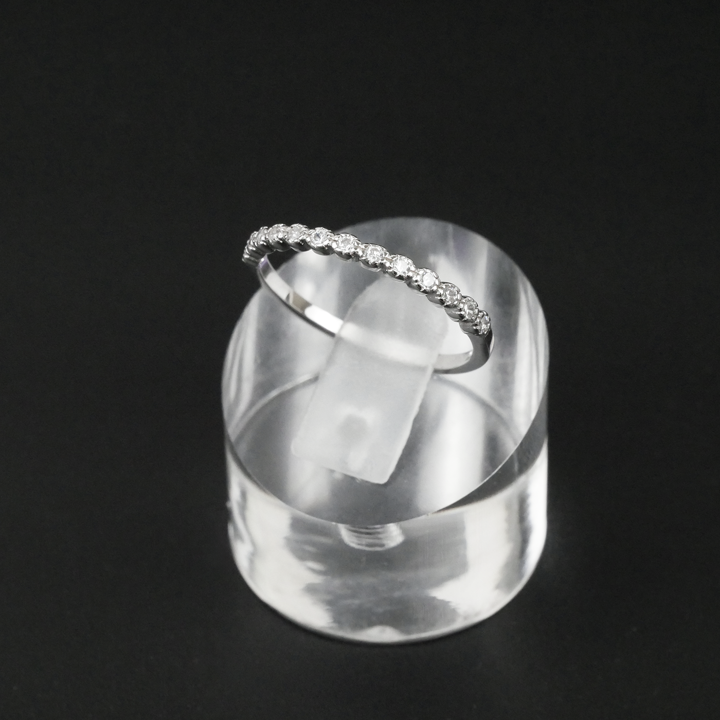 Silver ring with CZ's on a clear stand against a black background